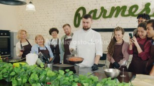 'Professional cook frying food teaching trainees while students clapping hands'