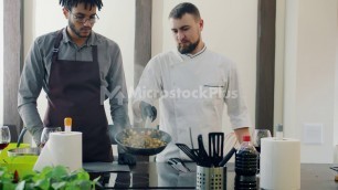 'Male chef teacher Afro-American trainee frying food in kitchen using pan'