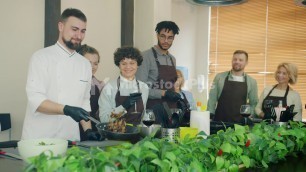 'Slow motion of young man chef frying food cooking meal teaching group of trainees'