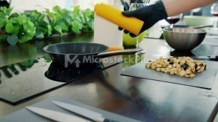 'Close-up of chef\'s hands in gloves frying food in fry pan in kitchen using modern appliances'