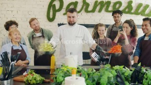 'Skilled chef teaching trainees frying food while people recording video clapping hands'