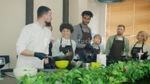 'Professional cook in uniform frying food teaching trainees in modern kitchen'